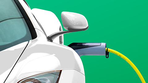 White electric car plugged into power socket with green backdrop.