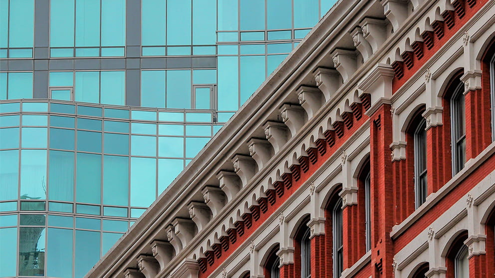 Close up of two buildings, one traditional red brick with intricate stonework, the second a modern glass skyscraper